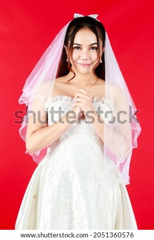 Asian happy bride in a white lace wedding dress smiling on red background.
