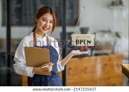 Asian Happy business woman is a waitress in an apron, the owner of the cafe stands at the door with a sign Open waiting for customers ,  cafes and restaurants Small business concept.