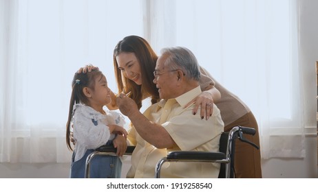 Asian Happy Disabled Elderly In Wheelchair With Daughter And Granddaughter Smiling Playing Together In Living Room At Home, Family Visit To Support Old Senior Man