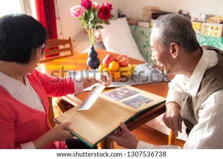 Asian happy elderly couple examines the album at home at the table and smiles.