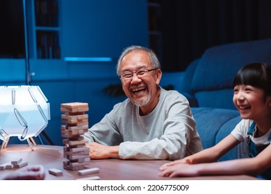 Asian Happy Family Of Little Daughter Play Toy Wooden Block In Home. Grandparents And Young Woman Loving Couple Parent Having Fun Play Stack Tower Wood Block Game At Night In Living Room.