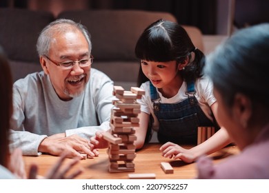 Asian Happy Family Of Little Daughter Play Toy Wooden Block In Home. Grandparents And Young Woman Loving Couple Parent Having Fun Play Stack Tower Wood Block Game At Night In Living Room.