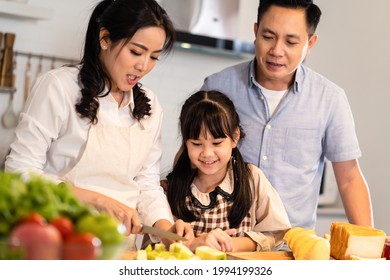 Asian Happy Family Making Food Preparation In Kitchen Room At House. Father, Mother And Children Having Fun Spending Time Together. Dad And Little Girl Looking At Mom Cooking Food. Family Relationship