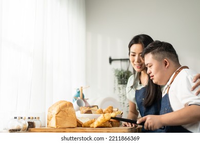 Asian Happy Family, Mature Mother Baking Bakery With Son In Kitchen. Attractive Beautiful Loving Parent, Mom Take Care And Teaching Young Man Cooking Food Breakfast Indoors At Home. Lifestyle Activity