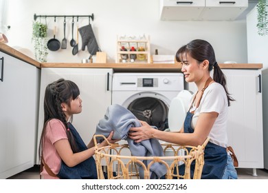 Asian Happy Family Stay Home, Mother Teach Daughter Wash Dirty Clothes. Young Little Cute Girl Child Help And Learn From Parent Mom To Put Laundry In Washer Appliance At Home. Domestic-Housekeeping.