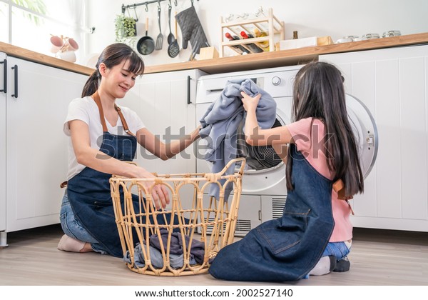 Asian happy family stay home,\
mother teach daughter wash dirty clothes. Young little cute girl\
child help and learn from parent mom to put laundry in washer\
appliance at home.\
Domestic-Housekeeping.