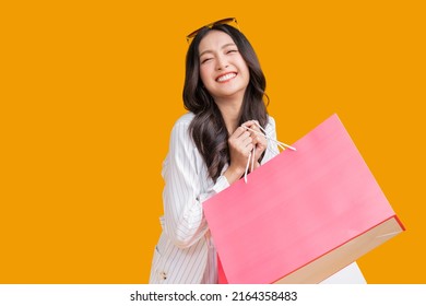 Asian happy female woman girl holds colourful shopping packages   standing on yellow background studio shot, Close up Portrait young beautiful attractive girl smiling looking at camera with bags - Shutterstock ID 2164358483