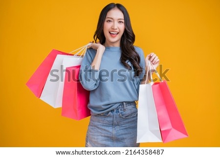 Asian happy female woman girl holds colourful shopping packages   standing on yellow background studio shot, Close up Portrait young beautiful attractive girl smiling looking at camera with bags