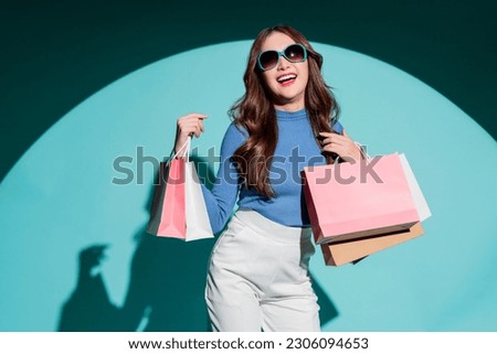 Asian happy female woman girl holds colourful shopping packages   standing on blue background studio shot, Close up Portrait young beautiful attractive girl smiling looking at camera with bags