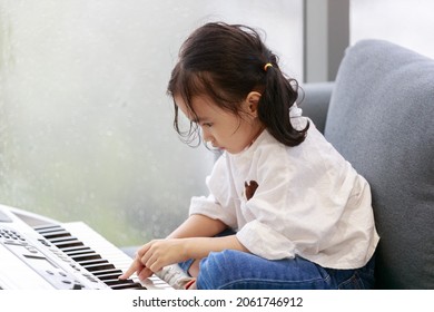 Asian Happy Girl Is Playing The Piano In A Music Practice Room, The Atmosphere Outside Is Raining. Water Droplets On The Glass. Concept Lovely Learning Education