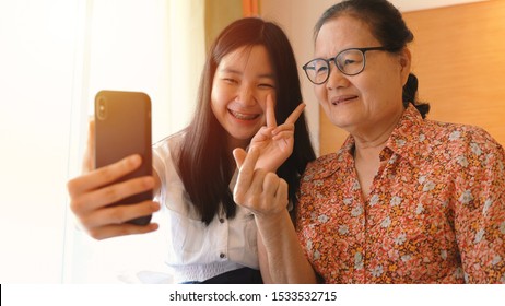 Asian Happy Grandmother And Her Granddaughter Having Fun While Using Smartphone And Taking Selfie Together Or Video Call And Facetime, Family And Technology Concept