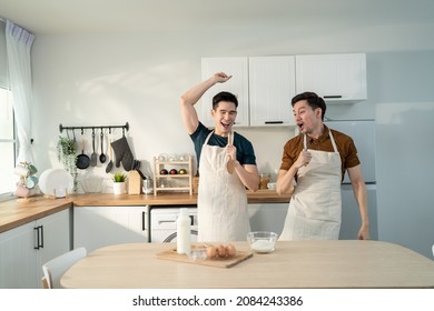 Asian Happy Handsome Man Gay Couple Sing And Dance Together In Kitchen. Attractive Romantic Male Lgbt Couple Wear Apron, Spending Free Leisure Time And Enjoy Listen To Music And Cooking Foods In House