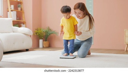 asian happy mother is leading her child son to stand on a weight scale and she encourage him by smiling about good body development - Powered by Shutterstock