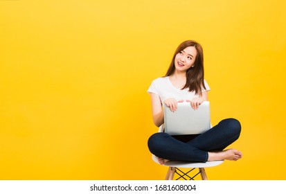 Asian Happy Portrait Beautiful Cute Young Woman Teen Smiling Sitting Crossed Legs On A Chair With Laptop Computer Looking To Side Isolated, Studio Shot On Yellow Background With Copy Space