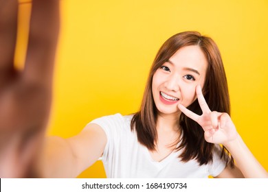 Asian Happy Portrait Beautiful Cute Young Woman Teen Smiling Standing Wear T-shirt Making Selfie Photo, Video Call On Smartphone Looking Camera Isolated, Studio Shot Yellow Background With Copy Space