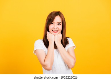 Asian happy portrait beautiful cute young woman teen stand wear t-shirt happy expression fist pressed together under chin looking to camera isolated, studio shot on yellow background with copy space