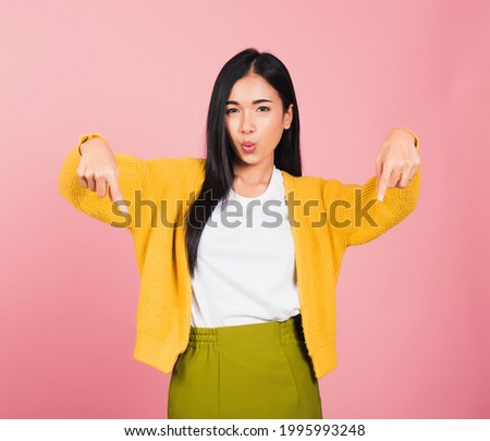 Asian happy portrait beautiful cute young woman smiling stand makes gesture two fingers pointing below down presenting and looking to camera, studio shot isolated on pink background with copy space