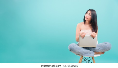Asian happy portrait beautiful young woman sitting on chair smile her  holding laptop computer and looking to side on blue background with copy space for text