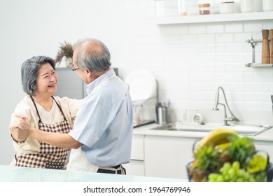 Asian Happy Senior Elderly Couple Standing In Kitchen At House Enjoy Retirement Life And Dancing Together. Loving Older Grandparents Cooking Foods With Smiling Face. Relationship And Activity At Home.