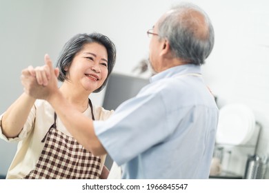 Asian Happy Senior Elderly Couple Standing In Kitchen At House Enjoy Retirement Life And Dancing Together. Loving Older Grandparents Cooking Foods With Smiling Face. Relationship And Activity At Home.