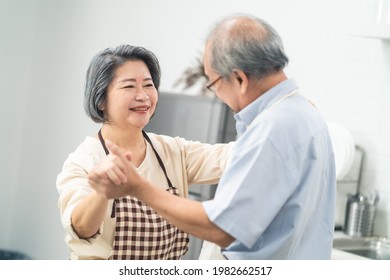 Asian Happy Senior Elderly Couple Standing In Kitchen At House Enjoy Retirement Life And Dancing Together. Loving Older Grandparents Cooking Foods With Smiling Face. Relationship And Activity At Home.