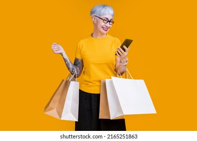 Asian happy senior female woman tattoo holds colourful shopping packages standing on yellow background studio shot, Close up Portrait old female hand hold smartphone enjoy shopping online cashless - Powered by Shutterstock