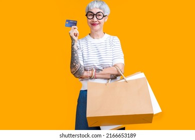 Asian Happy Senior Female Woman Tattoo Holds Colourful Shopping Packages Standing On Yellow Background Studio Shot, Close Up Portrait Old Female Hand Hold Shopping Bags Enjoy Shopping With Joyful