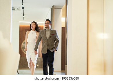 Asian happy upscale couple walking in hallway hand in hand smiling