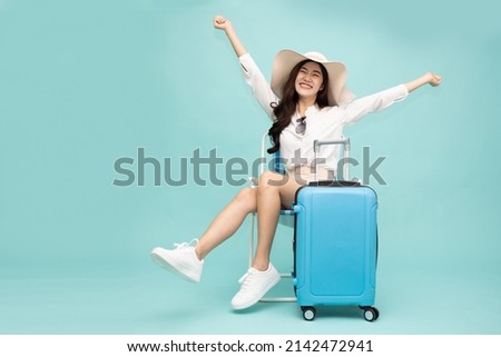 Asian happy woman sitting on chair with suitcase isolated on green background, Tourist girl having cheerful holiday trip concept