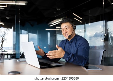 Asian with a headset is talking on video call, man inside office smiling and gesturing joyfully in an online meeting, a businessman is telling his colleagues, a customer service tech support worker. - Powered by Shutterstock