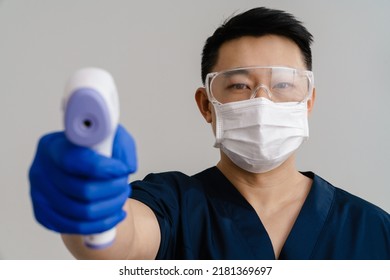 Asian Health Worker In Face Mask Using Forehead Thermometer Isolated Over White Background