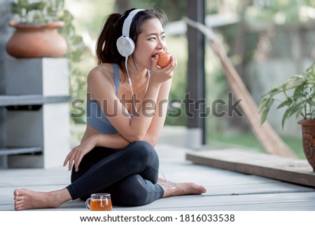 Asian healthy and sportive woman eating red apple while using headphone to listen music at home. Sport Concept.