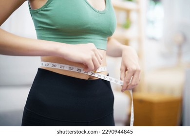 Asian healthy woman dieting Weight loss. Slim woman measuring waist with measure tape after diet at home weight control - Powered by Shutterstock