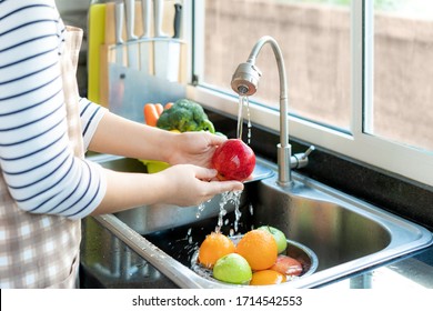 Asian healthy woman washing an apple and other fruit above kitchen sink and cleaning a fruit / vegetable with water to eliminate the chances of contamination COVID-19.