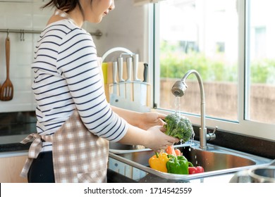 Asian healthy woman washing Broccoli and other vegetable above kitchen sink and cleaning a fruit / vegetable with water to eliminate the chances of contamination COVID-19.