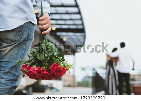 asian heartbroken man holding bouquet of red roses feeling sad while seeing woman dating with another man. broken heart, disappointed in love concept