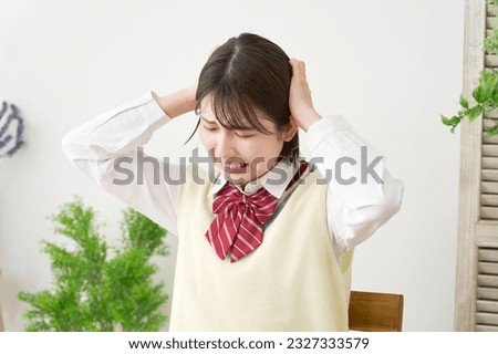 Asian high school student holding her head at home