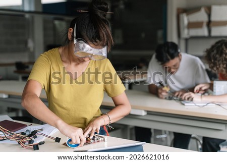 Asian High School teenage Student wearing protective goggles working on electronics circuit board in the science technology workshop - Digital Innovation in Education