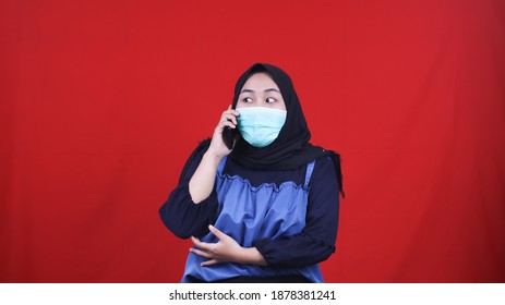 Asian hijab woman wearing mask calling friend isolated red background - Powered by Shutterstock