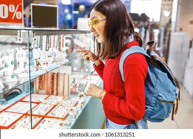 Asian Hipster Woman Chooses Jewelry In A Store And Looks At The Display Case