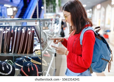 Asian Hipster Woman Chooses Jewelry In A Store And Looks At The Display Case