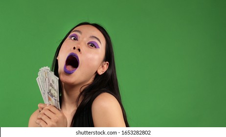Asian hipster young woman with american dollars in hands on an isolated green background.Surprise, shock,Joyful emotions, fun, laughter and happiness.