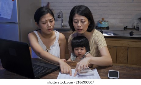 Asian Homosexual Couple With Their Adopted Child Are Going Through The Bank Statement While Calculating Monthly Home Expenses In The Dining Room.