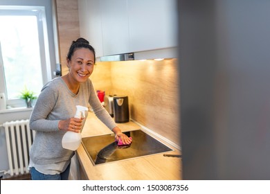 Asian Housewife Cleaning Furniture In Kitchen With Detergent. Glad Mature Asian Woman Wiping Surfaces At Home In Kitchen Interior. Woman Cleaning Kitchen. Woman Washing Kitchen Hood