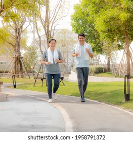 Asian Housewife And Husband Jogging Run In The Nature Park. Happy Middle Age Couple Smiling Exercise In Evening Summer. Married People Enjoy Running Outdoor Together. Man And Woman Healthy Lifestyle.