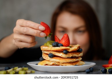 Asian Housewife Preparing Pancakes For Family, Putting Topping, Strawberries, Blueberris And Kiwi On Top.