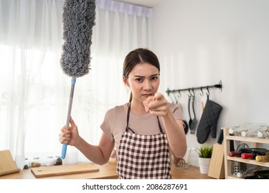 Asian housewife woman feel angry and need help with cleaning in house. Attractive beautiful maid housekeeper cleaner wearing apron and feather duster, pointing finger to camera with offended feeling.