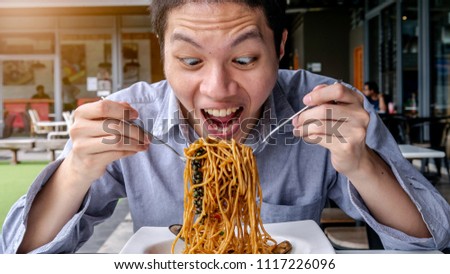 a Asian hungry man are open mouth ready to eating delicious Spaghetti with Spicy Mixed Seafood with fork an spoon on the white plate. He is enjoy eating and very happy with crazy strange face. 