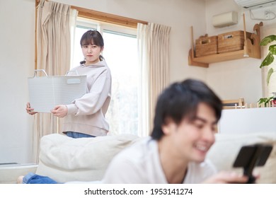 Asian husband playing games with wife doing housework - Shutterstock ID 1953141274