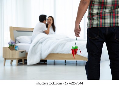 Asian Husband In Scottish Shirt Holding Heart Branch Seeing Wife And Male Adulterer On Bed In Bedroom